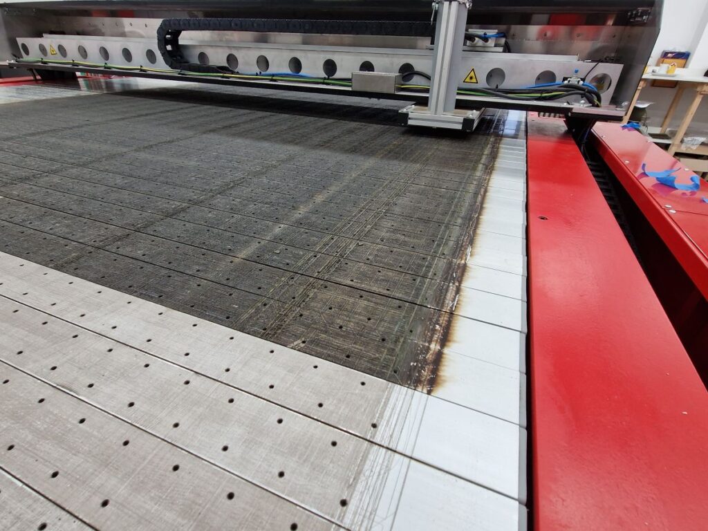 Pohled na laserový řezací stroj s podkladní plochou, kde je jasně vidět rozdíl před a po čištění laserem.